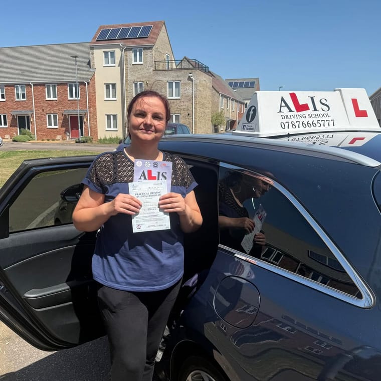 A pupil holding their practical driving test pass certificate beside Ali's car in King's Lynn.